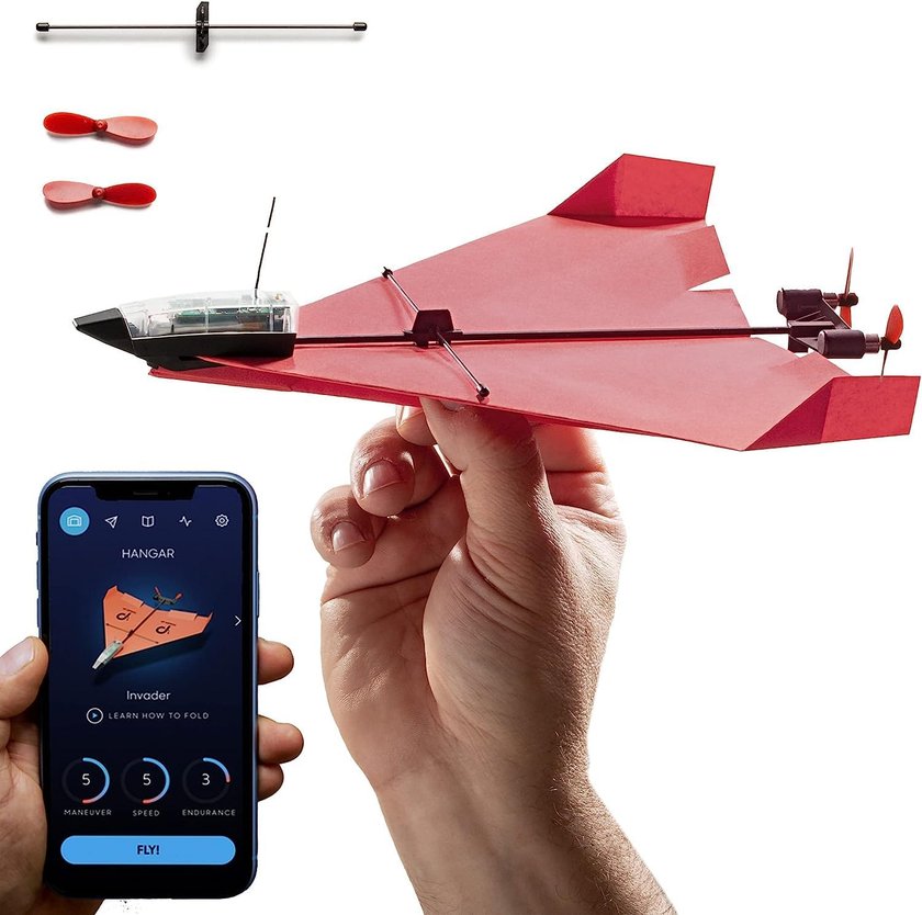 Eine Hand hält ein rotes Papierflugzeug mit einem kleinen Motor und Propellern. Daneben wird ein Smartphone mit einer App gezeigt, die das Flugzeug anzeigt. Auf dem Tisch liegen zwei zusätzliche rote Propeller und eine Montagevorrichtung für den Motor. Eine Hand hält ein rotes Papierflugzeug mit einem kleinen Motor und Propellern. Daneben wird ein Smartphone mit einer App gezeigt, die das Flugzeug anzeigt. Auf dem Tisch liegen zwei zusätzliche rote Propeller und eine Montagevorrichtung für den Motor.