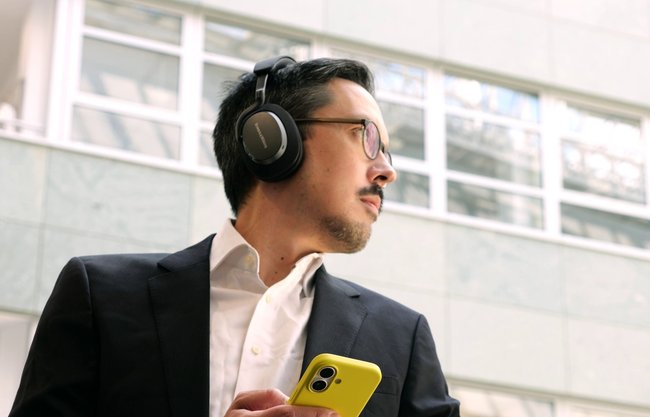 GIGA-Redakteur Stefan Bubeck trägt die schwarzen Over-Ear-Kopfhörer Bowers & Wilkins Px7 S3 und hält ein gelbes Smartphone. Im Hintergrund ist die Fassade eines modernen Gebäudes mit großen Fenstern zu sehen. GIGA-Redakteur Stefan Bubeck trägt die schwarzen Over-Ear-Kopfhörer Bowers & Wilkins Px7 S3 und hält ein gelbes Smartphone. Im Hintergrund ist die Fassade eines modernen Gebäudes mit großen Fenstern zu sehen.