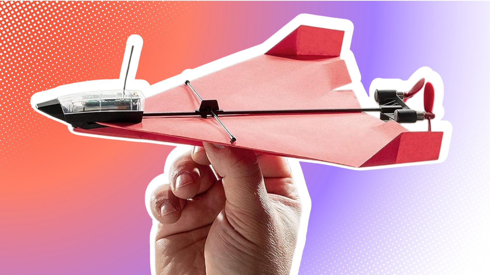 Eine Hand hält einen roten Papierflieger mit einem durchsichtigen Cockpit, das Elektronik und eine Antenne enthält. Der Flieger hat zwei Propeller am Heck. Eine Hand hält einen roten Papierflieger mit einem durchsichtigen Cockpit, das Elektronik und eine Antenne enthält. Der Flieger hat zwei Propeller am Heck.