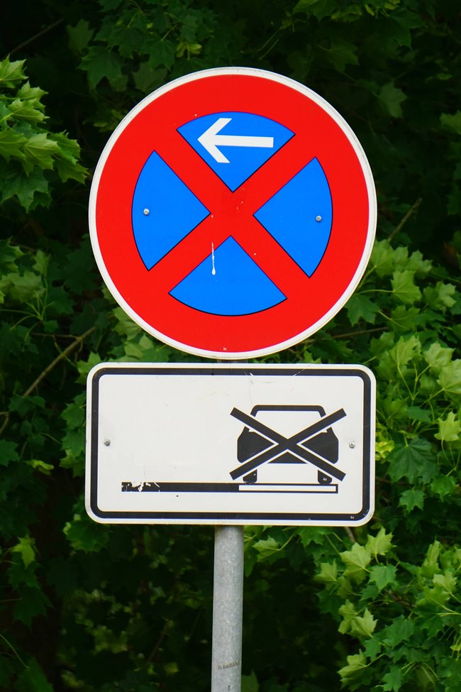 Blaues Schild mit rotem Kreuz und Pfeil nach links, darunter ein weißes Schild mit durchgestrichenem Auto. Blaues Schild mit rotem Kreuz und Pfeil nach links, darunter ein weißes Schild mit durchgestrichenem Auto.