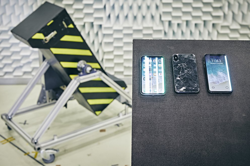 Streifen im Display und eine zerbrochene Rückseite: Das iPhone X hat den Falltest in der Trommel (Hintergrund) bei Stiftung Warentest nicht überlebt (Quelle: Stiftung Warentest)