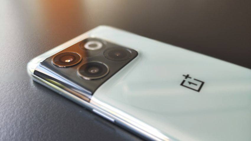 Das OnePlus 10T liegt mit dem Display auf einer schwarzen Tischplatte. Man sieht die helle Rückseite mit der Triple-Kamera.