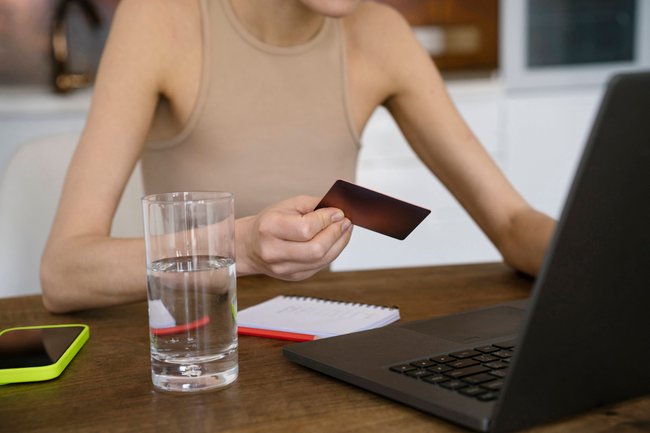 Eine Person sitzt vor einem Laptop und hat die Kreditkarte gezückt.