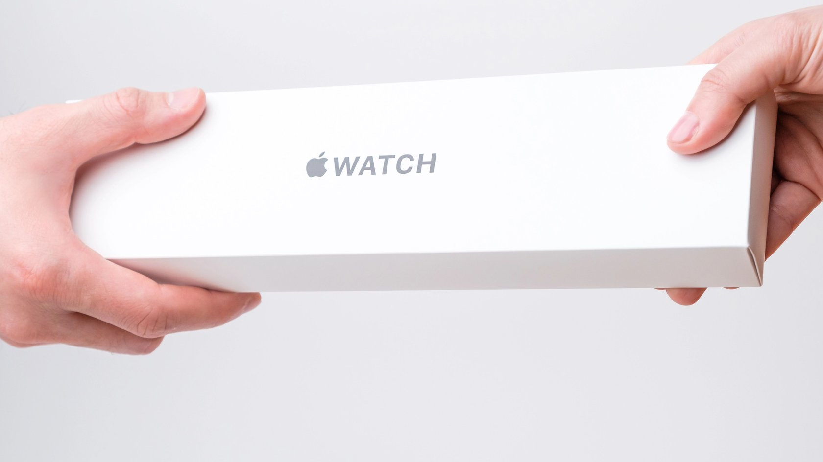 Mann und Frau Hand hält eine Box mit Apple-Uhr auf dem grauen Hintergrund.