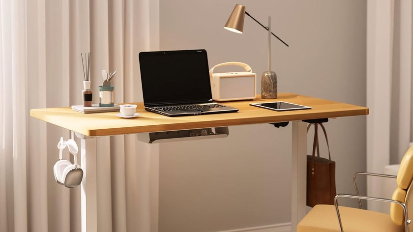 Höhenverstellbarer Schreibtisch mit Laptop, Schreibutensilien und Schreibtischlampe. 