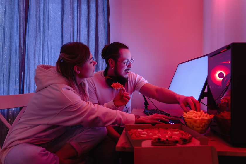 Junges Paar sitzt vor PC und isst Pizza und Chips.