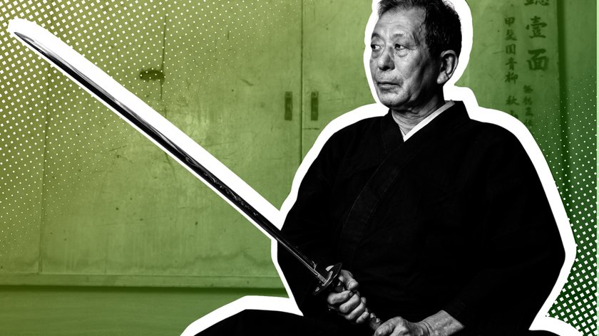 Schwarz-Weiss-Bild eines älteren Mannes in traditioneller Kampfkunst-Kleidung, der ein langes Schwert (Katana) vor sich hält. Der Mann sitzt mit ernstem Ausdruck, der Hintergrund ist in grünem Farbverlauf gehalten und zeigt asiatische Schriftzeichen an einer Wand.