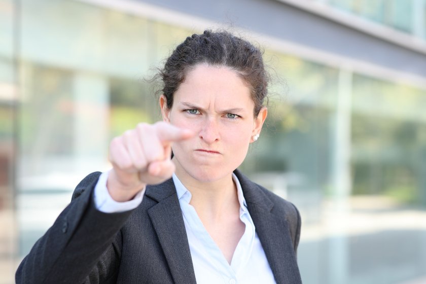 Frau schaut wütend in die Kamera und zeigt mit den Finger in die Kamera. 