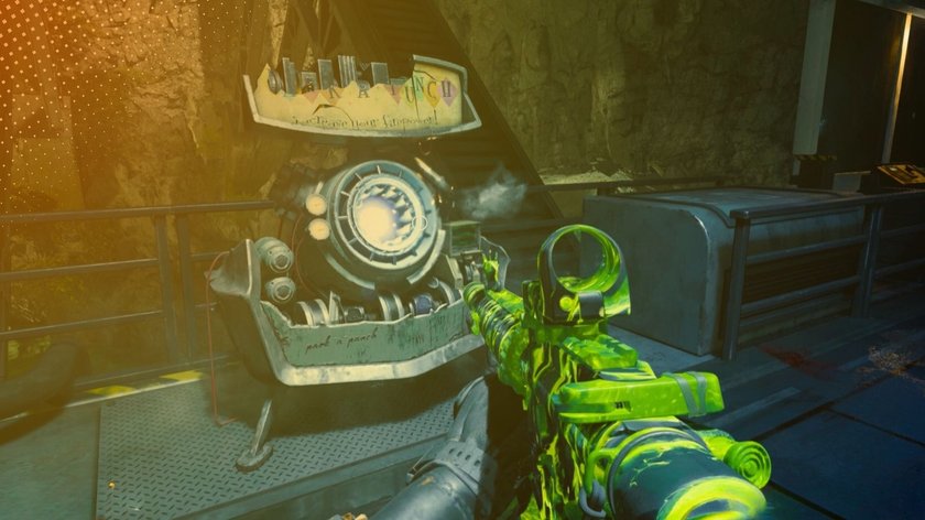 Ein Screenshot aus einem CoD: Black Ops 6 zeigt eine Waffe in Nahaufnahme mit einem neongrünen Tarnmuster, die auf eine futuristische Maschine mit der Aufschrift "Pack-a-Punch" gerichtet ist. Im Hintergrund ist eine felsige Höhlenwand sichtbar. Die Szene ist in gedämpftem Licht gehalten, was eine düstere Atmosphäre erzeugt.