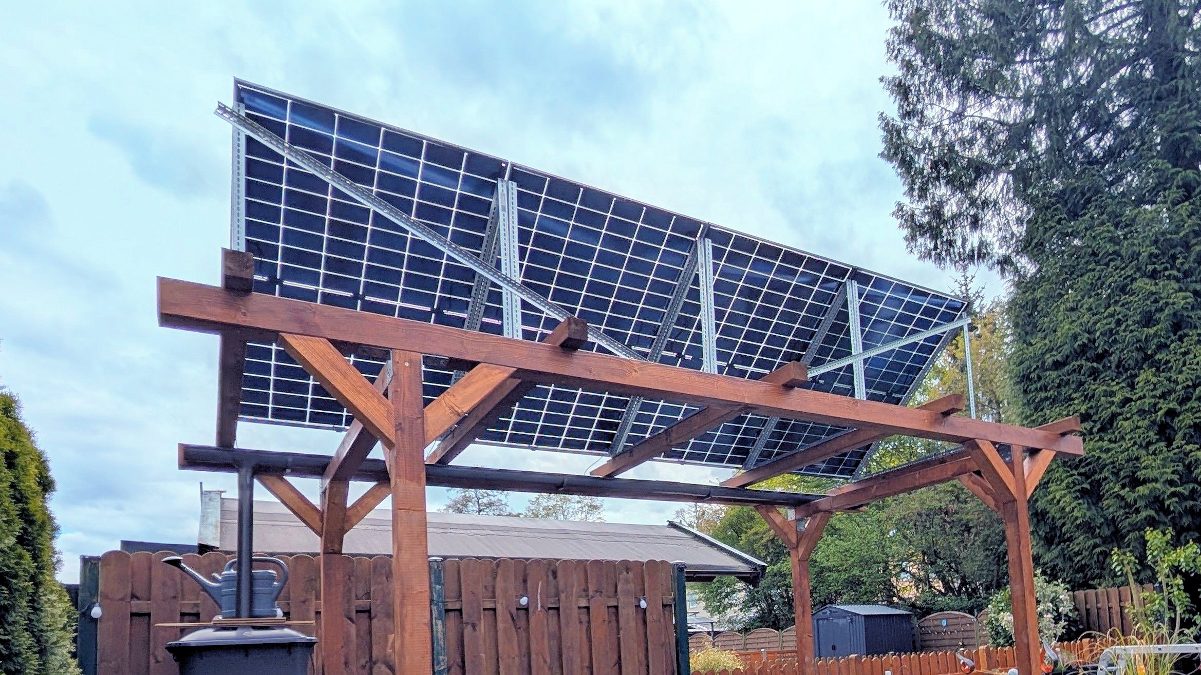 Aufnahme von 4 Solarmodulen, die auf einer Pergola in einem Garten aufgebaut sind.