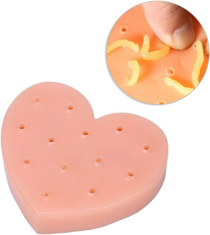 Ein herzförmiges, rosa Silikon-Spielzeug mit kleinen Löchern, das dazu dient, Pickel auszudrücken. Ein Detailbild zeigt, wie gelblicher Talg aus den Löchern gedrückt wird.