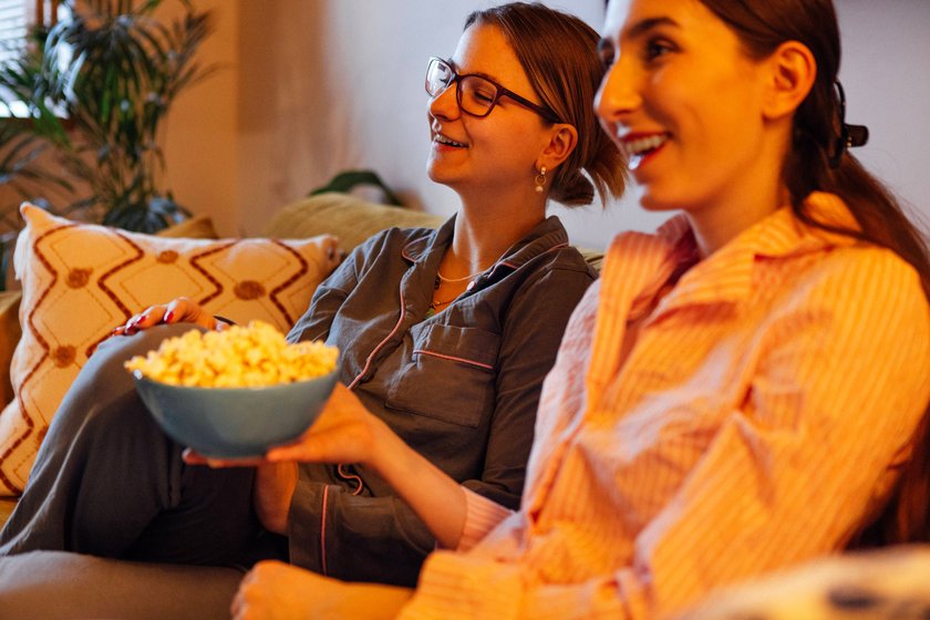Zwei junge Mädchen im Schlafanzug sitzen auf der Couch, schauen einen Film und essen Popcorn.