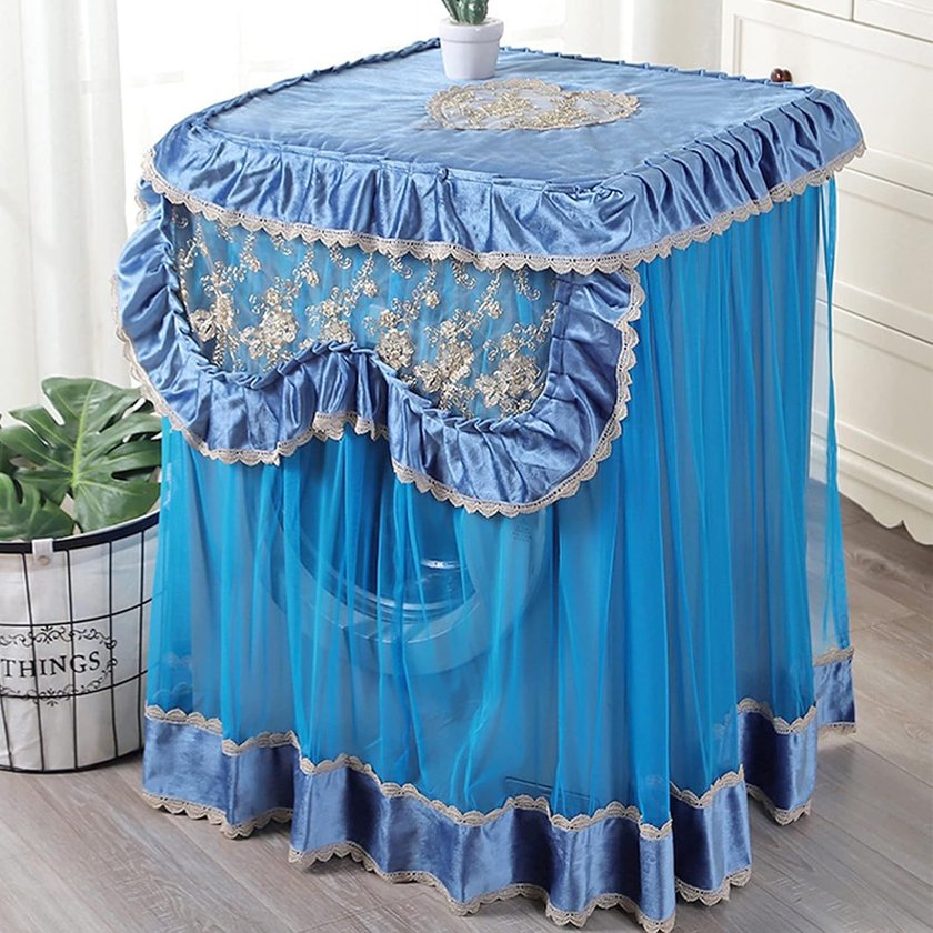 Blaue Waschmaschinenabdeckung mit Rüschen, Spitze und Blumenstickerei, darunter eine Waschmaschine sichtbar.