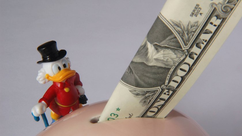 Dagobert Duck-Figur mit Dollarnote in einem Sparschwein.