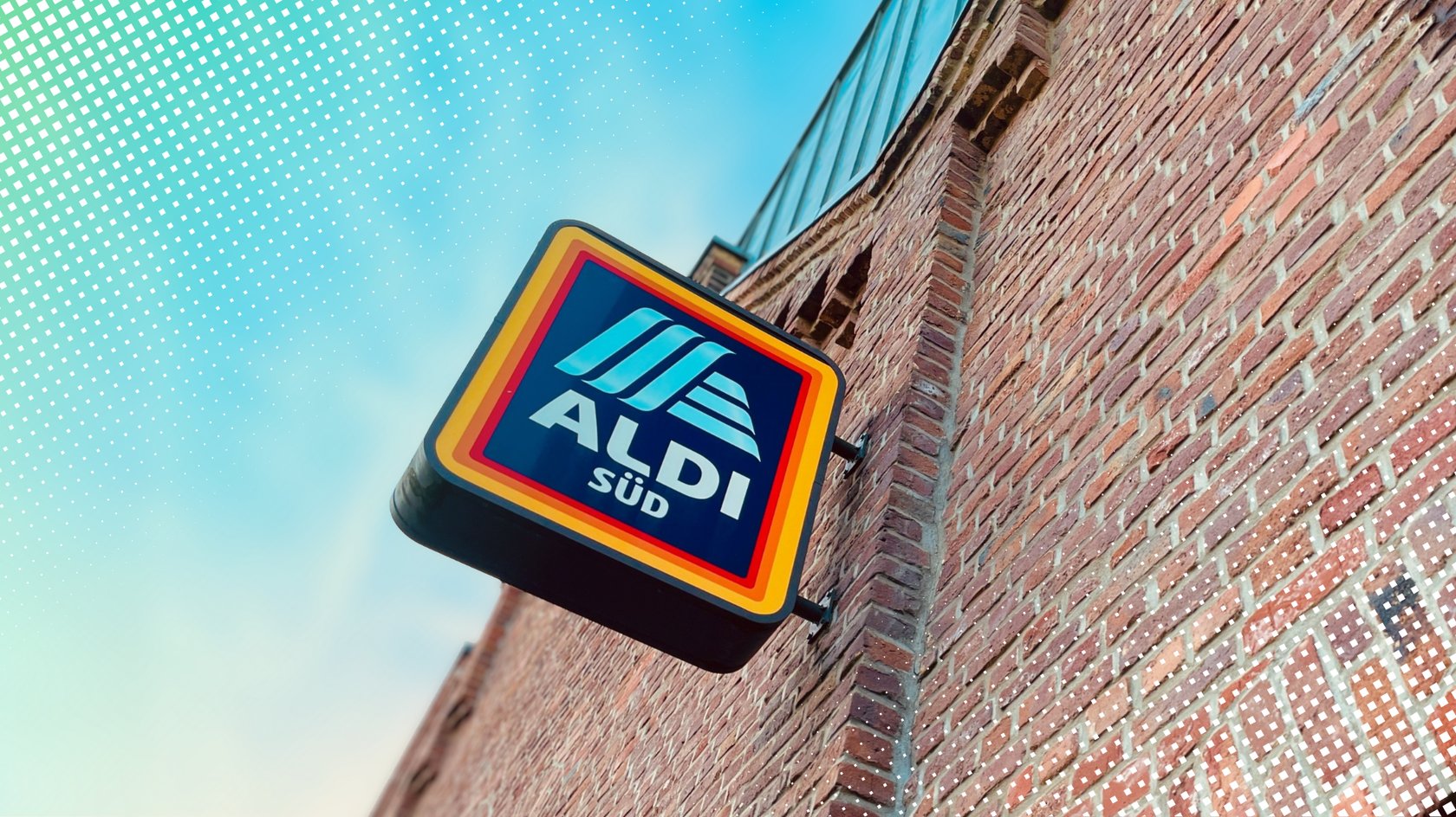 Ein quadratisches Aldi-Süd-Logo an einer roten Backsteinwand bei blauem Himmel.