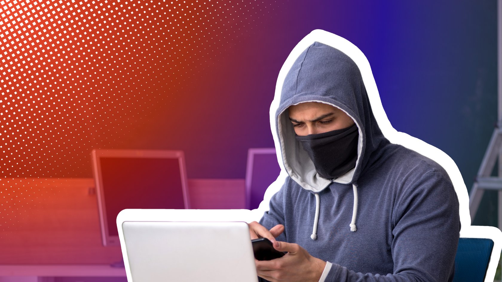 Ein Mann mit Kapuzenpullover und Gesichtsmaske sitzt an einem Schreibtisch mit einem Laptop und einem Smartphone in den Händen, im Hintergrund eine grüne Tafel und zwei Computermonitore.
