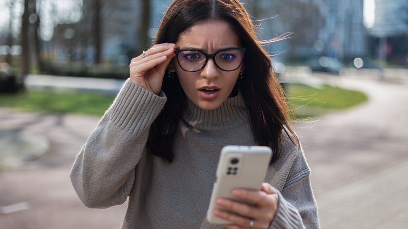 Junge Frau guckt überrascht auf ihr Handy