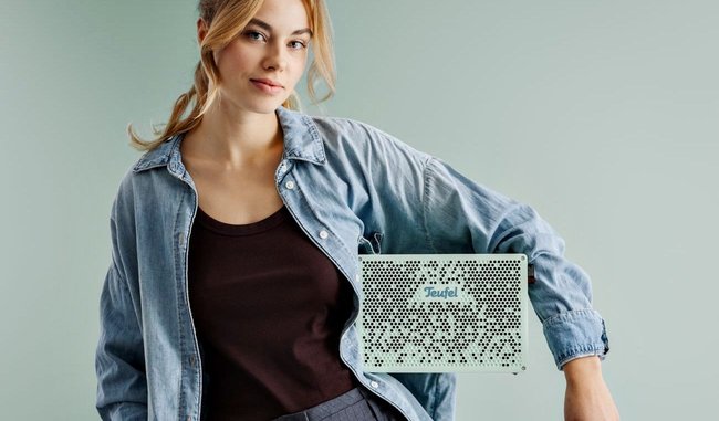 Der Bluetooth-Lautsprecher Teufel Mynd setzt auf recycelte Werkstoffe und austauschbare Komponenten. Hier zu sehen an einem weiblichen Model, das die hellgrüne Box unter dem linken Arm trägt.