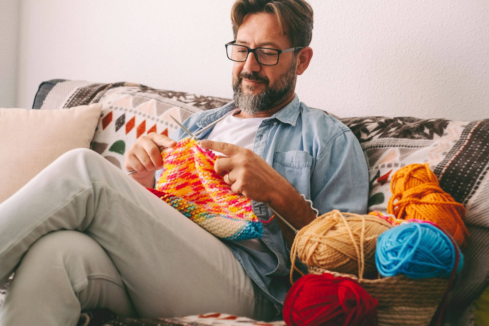 Mann sitzt strickend auf Couch