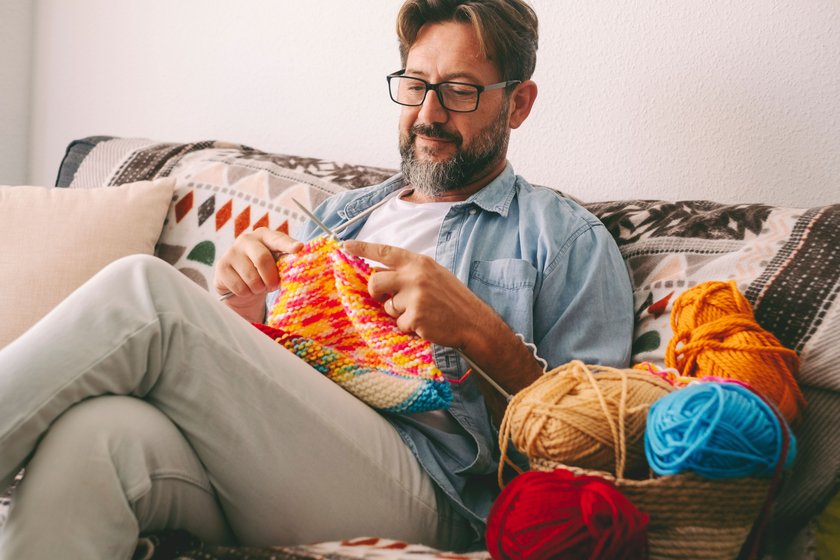 Mann sitzt strickend auf Couch