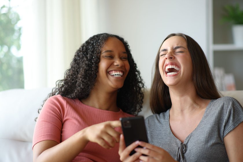 Zwei Frauen schauen gemeinsam auf Handy und lachen