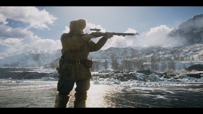 Mann steht in schneebedeckter Landschaft und zielt mit Waffe auf etwas in der Ferne.