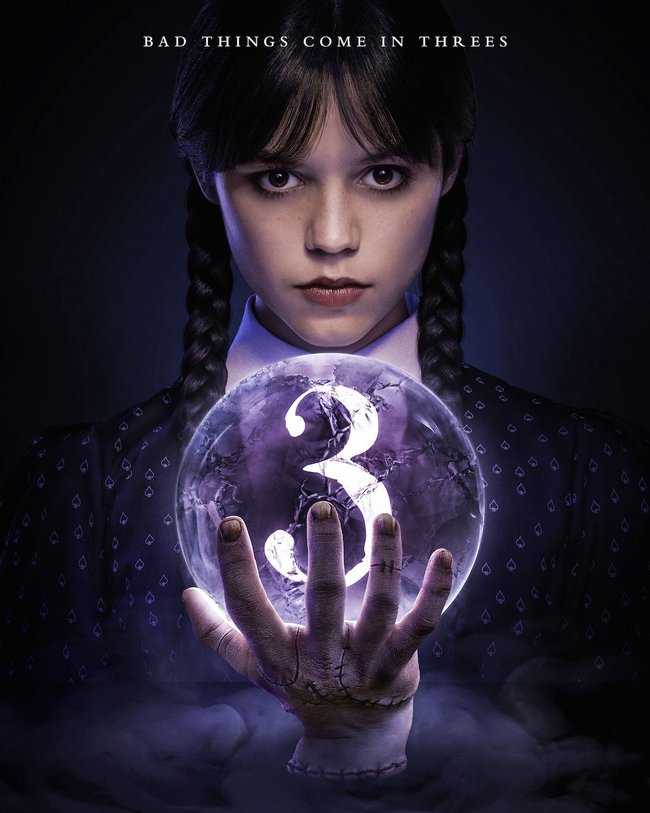 Ankündigungsbild für Staffel 3 von Wednesday, bei der man das Gesicht der Hauptdarstellerin (Jenna Ortega)hinter einer Kristallkugel mit der Zahl "3" drin sieht, welche vom Eiskalten Händchen gehalten wird.