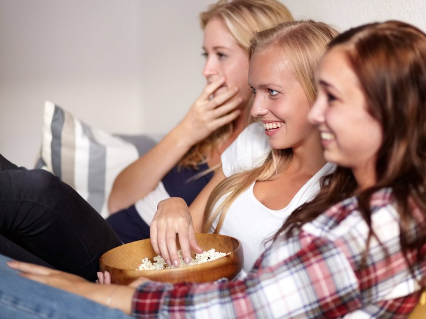 Drei Frauen sitzen lachend auf dem Sofa und schauen fern.