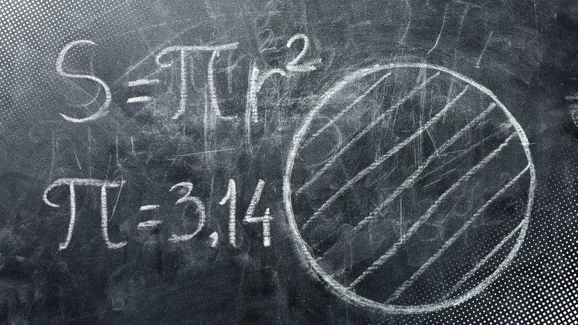 Kreidetafel mit mathematischen Formeln und einer gezeichneten Kreisfläche: Links steht "S = πr²" und darunter "π = 3,14". Rechts ist ein mit Schraffuren gefüllter Kreis skizziert.