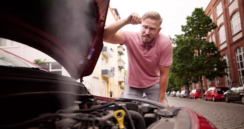 Mann schaut frustriert in die Motorhaube eines defekten Autos. 