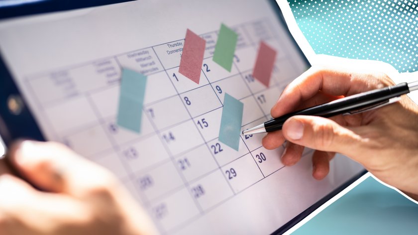 Mensch hält Kalender mit der linken Hand und macht mit der rechten Hand, in der die Person einen Stift hält, notizen