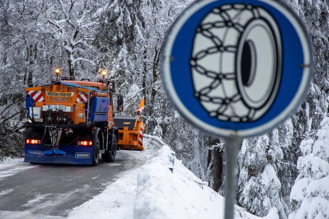 Schmitten, Hessen: Die verschneite Landschaft am Großen Feldberg im Taunus. Links ein Schneefahrzeug zu sehen. Rechts das Verkehrszeichen für Schneekettenpflicht.