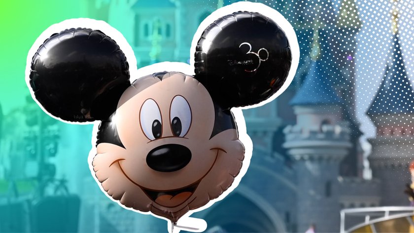 Schwarzer Mickey-Mouse-Ballon mit einem lächelnden Gesicht in der Mitte und grossen runden Ohren. Auf einem Ohr ist die Zahl „30“ mit dem Schriftzug „Disneyland“ zu sehen. Der Hintergrund zeigt ein verschwommenes Schloss, möglicherweise das Disneyland-Schloss, mit einem Farbverlauf von Blau zu Grün und weissen Punkten am rechten Rand.