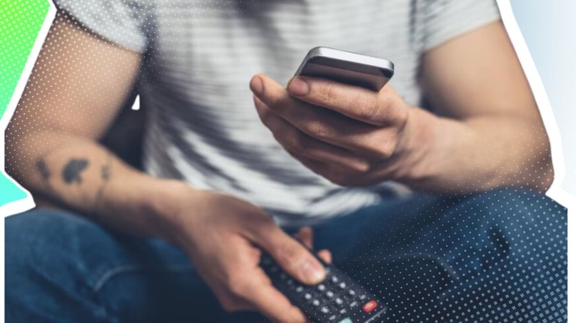 Mann mit Smartphone in der einen und Fernbedienung in der anderen Hand 