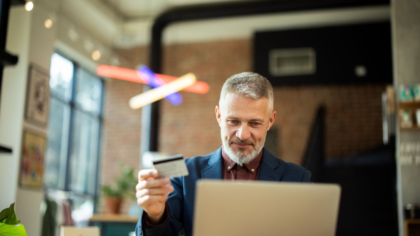 Focused mature businessman is holding a credit card and making an online payment on a laptop in a cafe