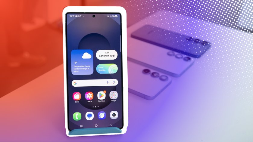 Ein modernes Smartphone (Samsung Galaxy S25) dessen Display aktiv ist und verschiedene Widgets sowie Apps anzeigt, darunter eine Wettervorhersage mit -1°C für Berlin und die Nachricht „Schönen Tag!“. Im Hintergrund sind unscharf weitere Smartphones auf einem Tisch sichtbar. Der Hintergrund des Bildes ist mit einem roten und violetten Farbverlauf sowie einem Punktmuster gestaltet.