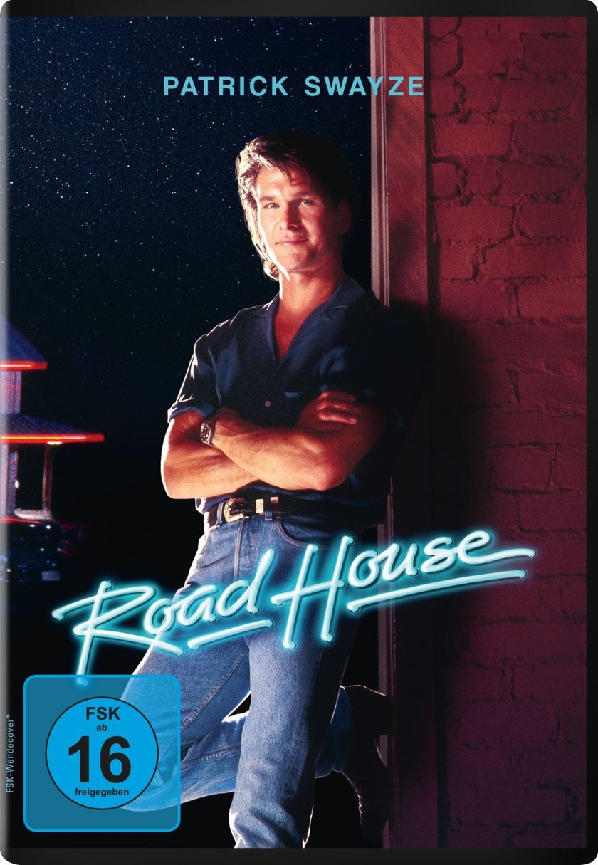 Filmplakat für „Road House“ mit Patrick Swayze. Er steht lässig an eine Ziegelwand gelehnt, die Arme verschränkt und trägt ein blaues Hemd und Jeans. Der Hintergrund zeigt einen sternenklaren Nachthimmel und die Lichter eines Gebäudes. Der Filmtitel „Road House“ ist in leuchtend blauen Neonbuchstaben dargestellt.