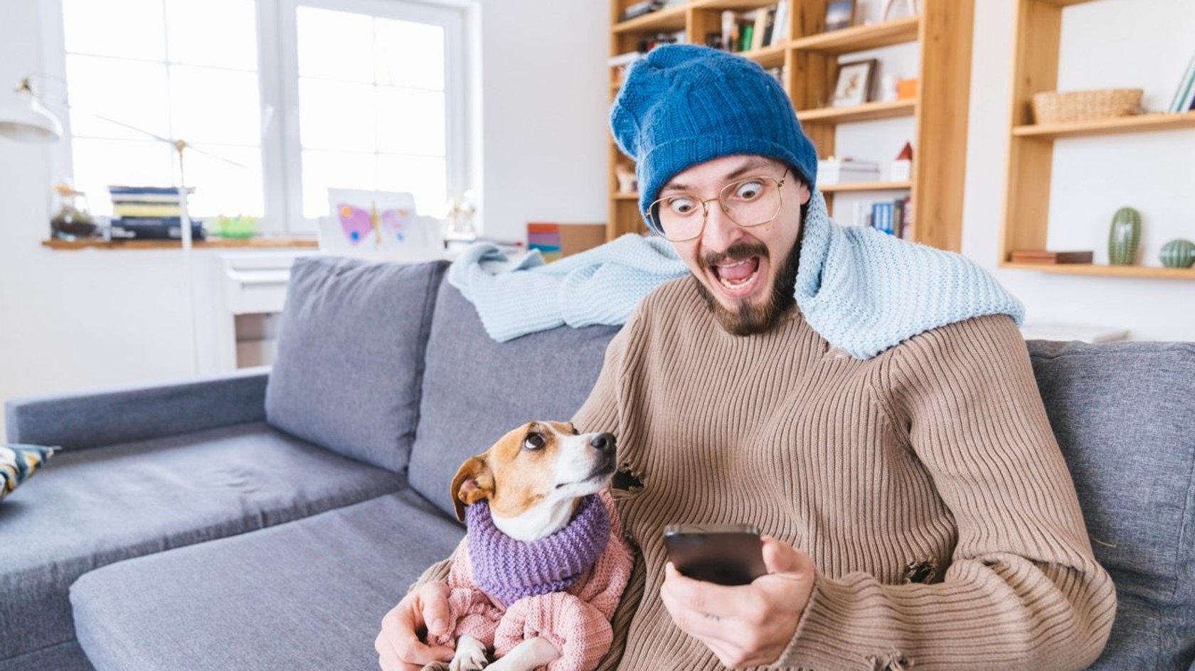 Mann mit iPhone sitzt erschrocken auf der Couch.