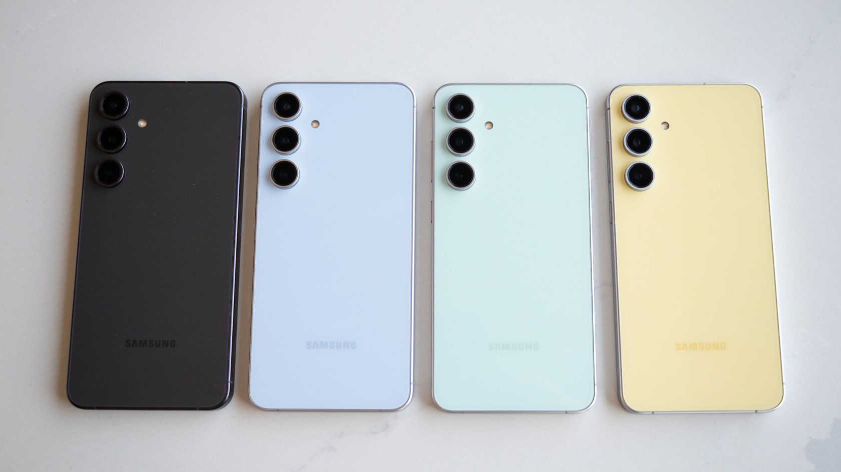 Vier Samsung-Galaxy-Handys, die nebeneinander auf einem Tisch liegen und unterschiedliche Farben haben.