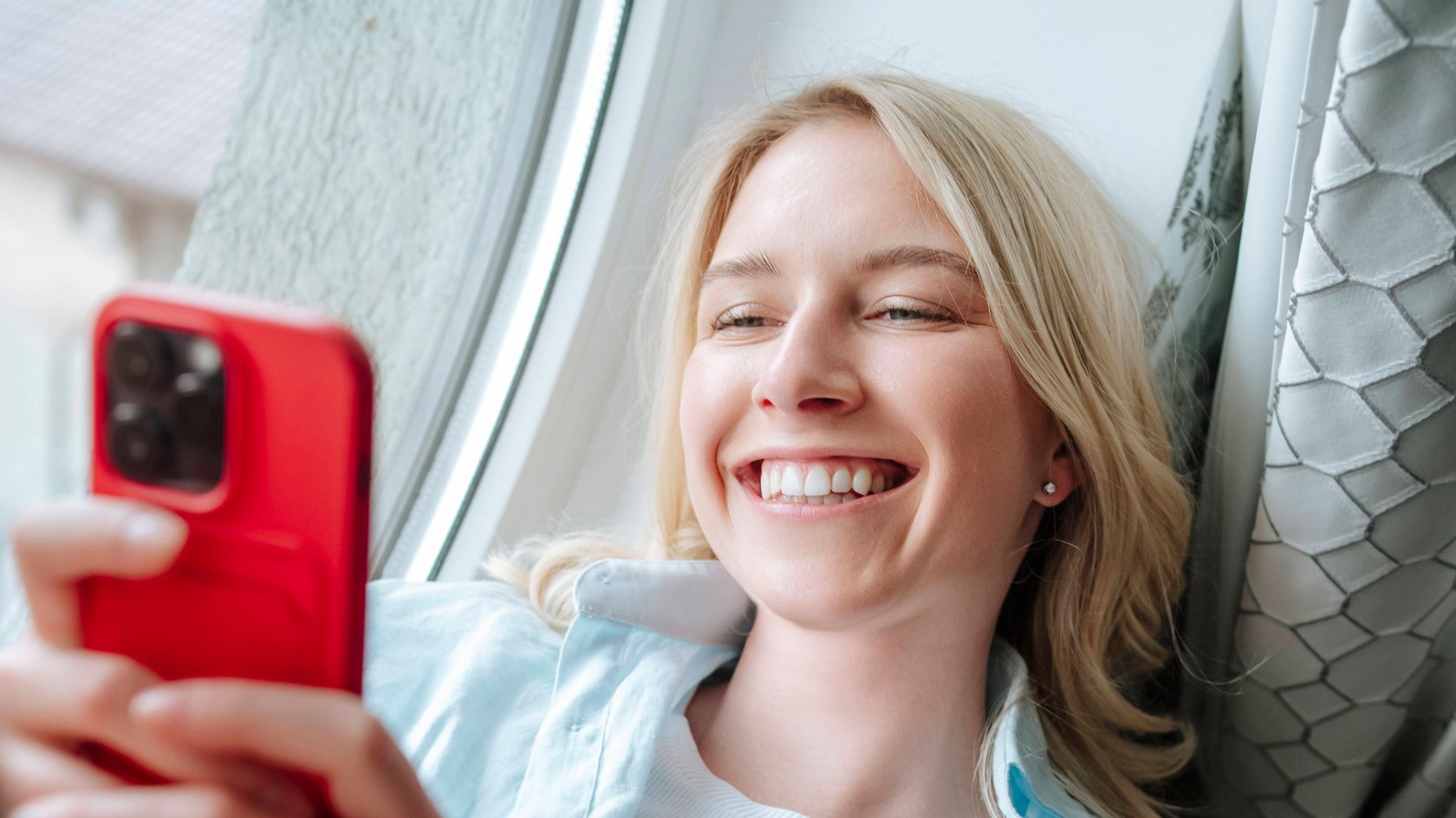 Happy beautiful woman using smart phone on window sill at home model released, Symbolfoto, MDOF02674
