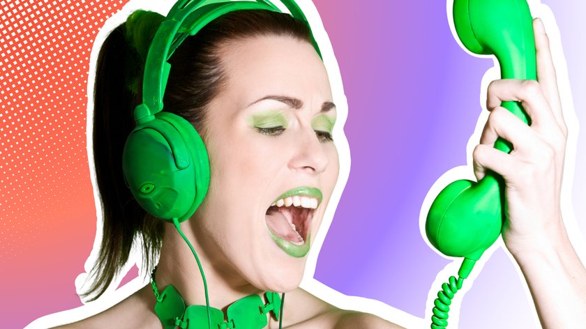 Eine Frau mit grünem Make-up, Kopfhörern und einer Halskette schreit in ein grünes Retro-Telefon vor einem grünen Hintergrund.