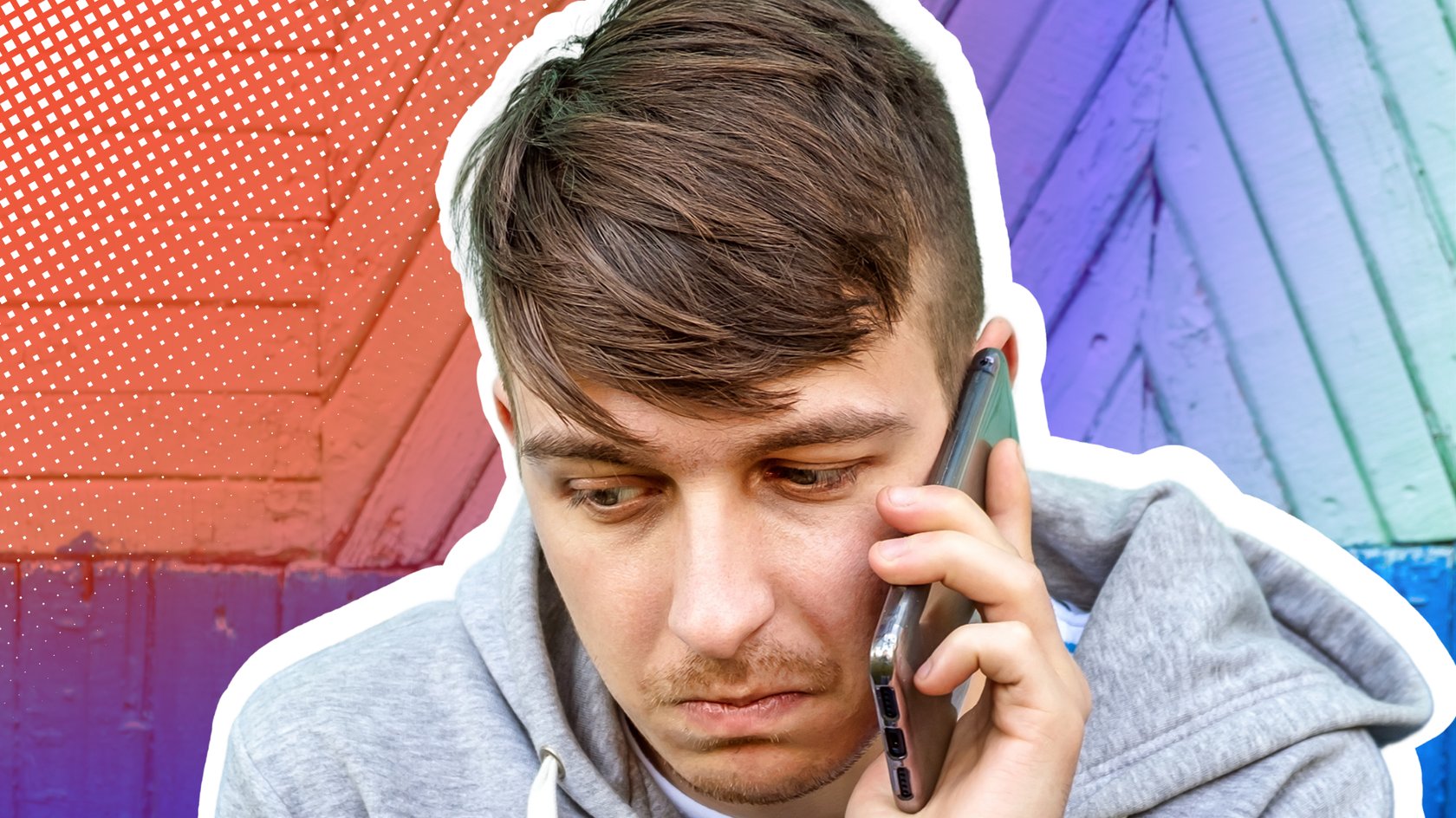 Ein junger Mann mit braunen Haaren und einem grauen Kapuzenpullover telefoniert mit einem Smartphone vor einer blau-türkis gestrichenen Holzwand und blickt dabei nach unten.