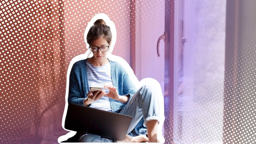 Frau mit Laptop und Smartphone sitzt auf der Fensterbank