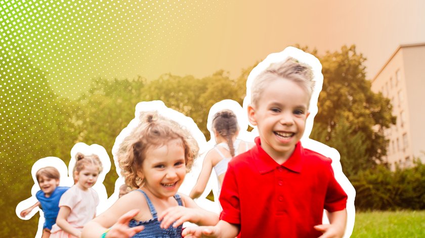 Eine Gruppe von Kindern spielt lachend im Freien auf einer Wiese. Im Vordergrund sind ein Junge in einem roten Polohemd und ein Mädchen in einem blauen Kleid zu sehen, die fröhlich rennen. Im Hintergrund sind weitere Kinder sowie Bäume und ein Gebäude zu erkennen.