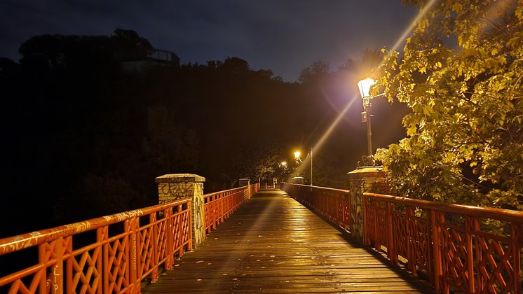 Eine Brücke mit rotem Geländer wird bei Nacht von Laternen beleuchtet.