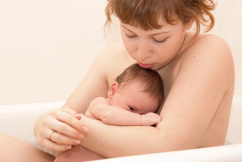 Serious mother with her newborn baby taking bath. Mother holding her baby. Selective focus on mothers and baby faces