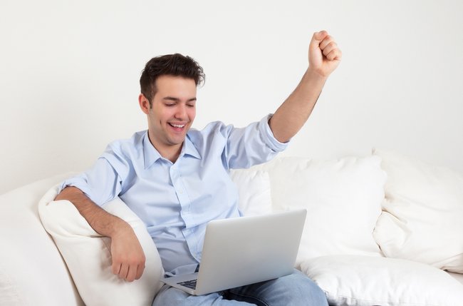 Cheering hispanic guy with notebook on a sofa