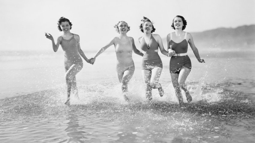 Was ist Vintage? Vier Frauen rennen ausgelassen am Strand in Retro-Bademode