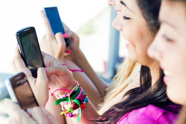 three girls chatting with their smartphones at the park