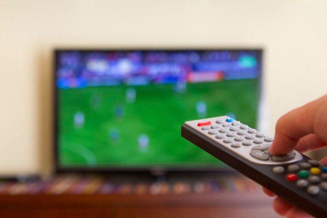 Watching a soccer match in the television, with a tv remote control in the hand